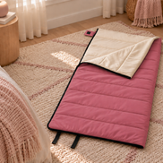 Pink junior organic cotton sleeping bag laid out on a rug beside a bed in a child's bedroom