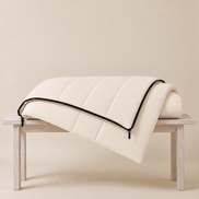 Undyed organic cotton sleeping bag folded over a wooden bench, showing its soft quilted channels