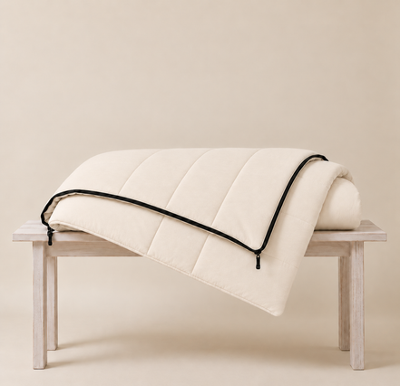 Undyed organic cotton sleeping bag folded over a wooden bench, showing its soft quilted channels